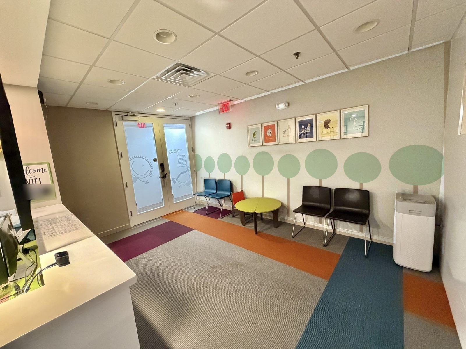 Bright waiting room with colorful carpet, kid-sized table and chairs, and framed children's art